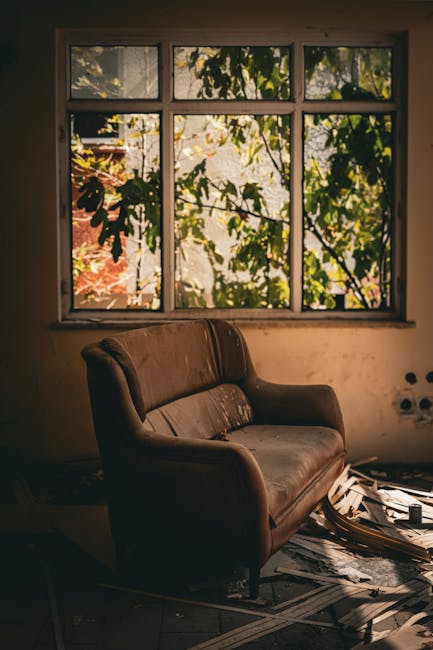 A three-seater sofa with a fabric upholstery in a textured grey material positioned outdoors against a brick wall. The sofa has four back cushions, each with button tufting, and three seat cushions, o